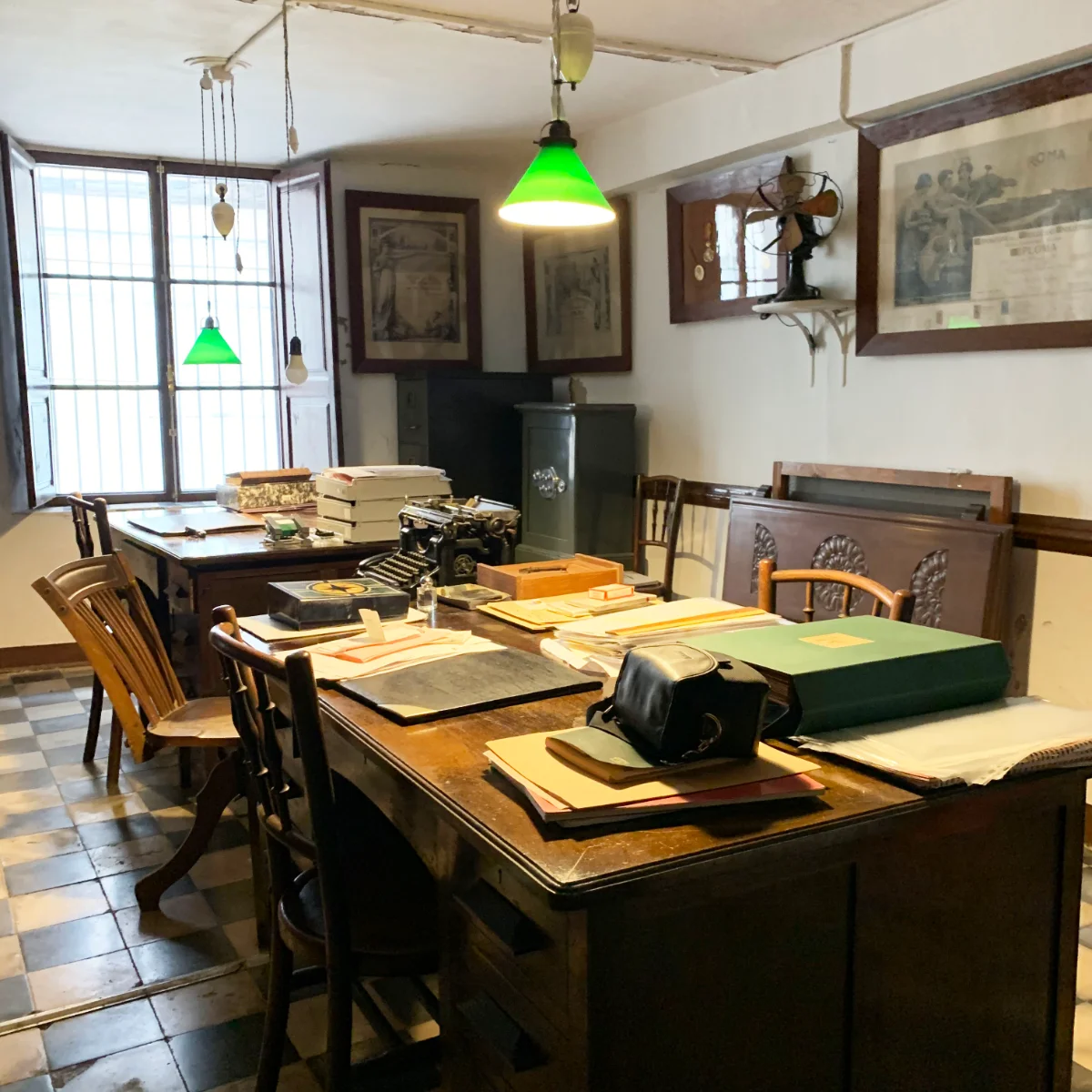 Despacho antiguo con escritorio de madera, máquina de escribir, lámparas verdes y diplomas enmarcados